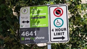 Close up of a parking sign, indicating the parking enforcement rules for the area as well as indicating the location of the accessible parking stall in the lot.