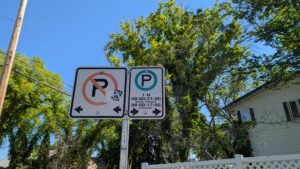 Close up of street signs indicating parking enforcement rules,with the area to the right of the sign designated for one-hour street parking, while all parking is prohibited to the left of the sign. 