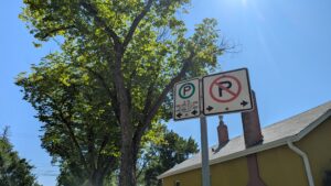 Close up of street signs indicating parking enforcement rules, with the area to the left of the sign designated for two-hour street parking, while all parking is prohibited to the right of the sign. 